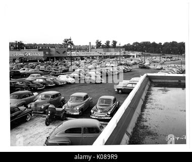 Photographie de l'aire de stationnement pour le centre commercial Northwood à Baltimore, Maryland, montrant de nombreuses voitures et bâtiments commerciaux tels que l'Acme Markets, S S Kresge Company, et le théâtre de Northwood, avec des immeubles d'habitation et arbres en arrière-plan, Baltimore, Maryland, le 14 juin 1951. Banque D'Images