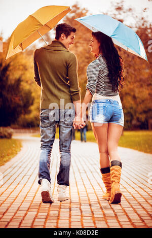 Quel beau couple magnifique avec parasols bénéficiant en marchant sous la pluie à travers le parc en automne couleurs. vue arrière. Banque D'Images