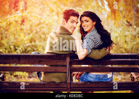 Belle lovely couple assis sur le banc et profiter à sunny park en couleurs de l'automne. looking at camera. vue arrière. Banque D'Images