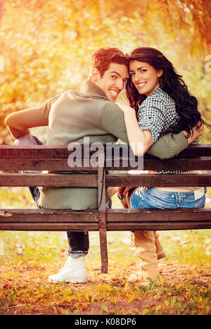Belle lovely couple assis sur le banc et profiter à sunny park en couleurs de l'automne. looking at camera. vue arrière. Banque D'Images