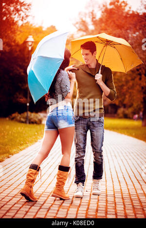 Quel beau couple magnifique avec parasols bénéficiant en marchant sous la pluie à travers le parc en couleurs de l'automne. Banque D'Images