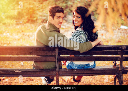 Belle lovely couple assis sur le banc et profiter à sunny park en couleurs de l'automne. looking at camera. vue arrière. Banque D'Images