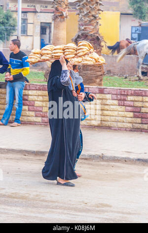 Femme porte un plateau sur sa tête avec du pain frais, peuple égyptien sur la rue au Caire, en Egypte. Banque D'Images