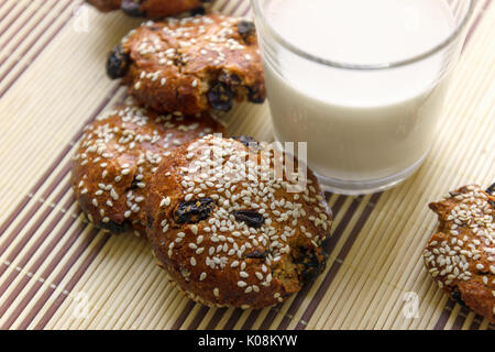 Des biscuits sur la table avec des graines de sésame, les raisins secs et un verre de lait Banque D'Images