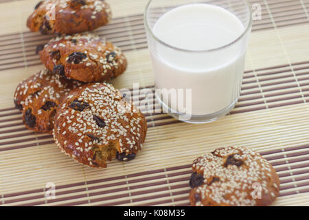 Des biscuits sur la table avec des graines de sésame, les raisins secs et un verre de lait Banque D'Images