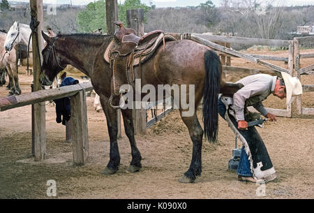 Un maréchal-ferrant mâle vers le bas les fichiers d'un sabot de cheval avant de clouer sur les nouveaux fers dans un ranch de l'Ouest qui dispose de sentiers pour les cowboys et cowgirls en Arizona, USA. Banque D'Images