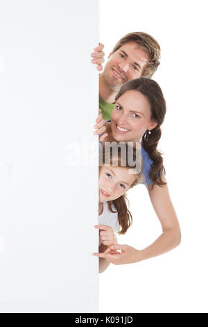 Portrait de famille heureuse peeking de blank billboard sur fond blanc Banque D'Images