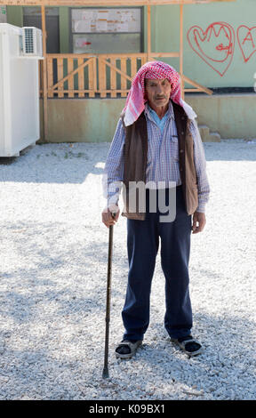 À Ritsona camp de réfugiés pour les Syriens. Un vieil homme syrienne soutenue par un bâton de marche se place en avant d'un bâtiment avec des graffitis. Banque D'Images