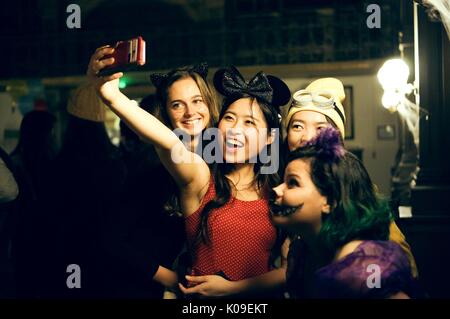 Un groupe de quatre étudiants du collège des femmes vêtues de costumes ; un étudiant comme Minnie Mouse tenant une prendre un, un autre étudiant selfies vêtu de la pourpre, vert, et la peinture pour le visage du Joker, un étudiant sur le dos habillé comme un Minion, et l'élève la plus à gauche portant des oreilles de chat et chat ; maquillage toutes les expressions du visage souriant, avec l'Halloween à la bibliothèque de Peabody, Johns Hopkins University, 31 octobre 2015. Avec la permission de Eric Chen. Banque D'Images