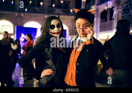 Deux étudiants posant avec leurs bras autour de l'autre, la fille porte tout noir et a maquillage visage sur dans le style du caractère le Joker, elle a un grand sourire rouge et noir autour de ses yeux et le garçon porte des oreilles orange, verres et une orange et noir, 2015. Avec la permission de Eric Chen. Banque D'Images