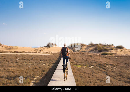Homme avec chien marcher sur le chemin en bois sur la plage et à la recherche dans la distance de l'océan Banque D'Images