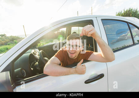 Portrait of happy smiling young man, acheteur assis dans sa nouvelle voiture et montrant les clés en dehors du bureau du concessionnaire. Les déplacements personnels, auto concept achat Banque D'Images