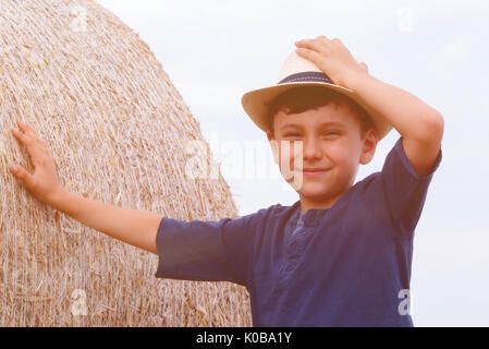 Jeune garçon de pays dans la région de hat près de meules au coucher du soleil en été. Concept d'été, des vacances actives à l'extérieur.Les loisirs avec les enfants lors des chaudes journées d'été. Banque D'Images