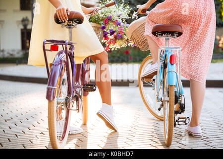 Vue arrière de deux filles en robes assis sur un vélo vintage en plein air Banque D'Images