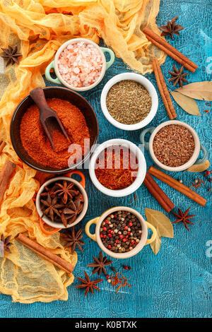 Epices et condiments colorés secs anis, paprika, Safran, poivre, sel, le laurier, la cannelle dans de petits bols sur fond bleu Banque D'Images