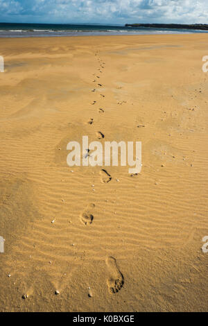 Marcher seule sur la plage. Des traces de pas dans le sable, le ciel bleu, légèrement nuageux, la marée. Falaises d'arrière-plan. Banque D'Images