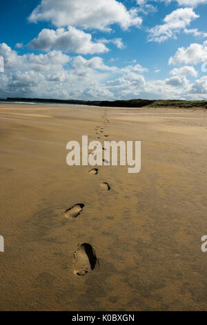 Marcher seule sur la plage. Des traces de pas dans le sable, le ciel bleu, légèrement nuageux, la marée. Falaises d'arrière-plan. Banque D'Images