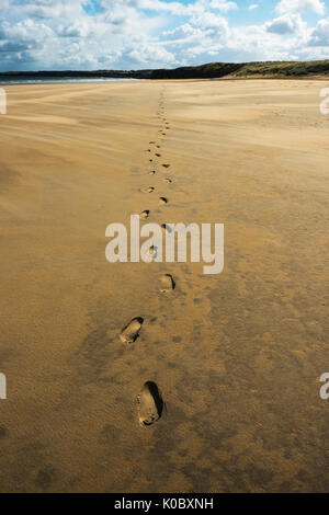 Marcher seule sur la plage. Des traces de pas dans le sable, le ciel bleu, légèrement nuageux, la marée. Falaises d'arrière-plan. Banque D'Images