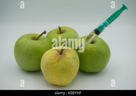 1 apple injecté jaune en face de 3 pommes vertes sur fond blanc. Banque D'Images