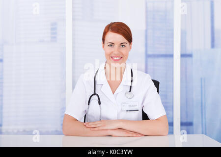 Portrait de belle jeune femme médecin sitting at desk in clinic Banque D'Images