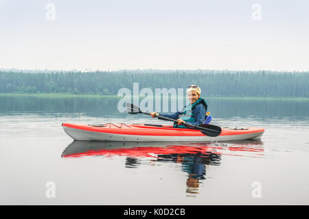 Femme heureuse de pagayer de red kayak sur lac calme, Alberta, Canada Banque D'Images