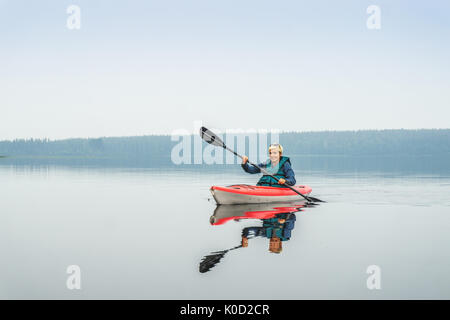 Femme heureuse de pagayer de red kayak sur lac calme, Alberta, Canada Banque D'Images