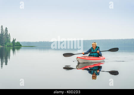 Femme heureuse de pagayer de red kayak sur lac calme, Alberta, Canada Banque D'Images
