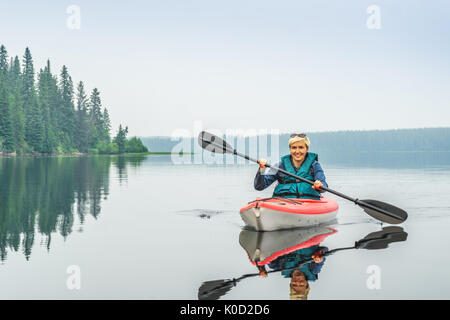 Femme heureuse de pagayer de red kayak sur lac calme, Alberta, Canada Banque D'Images