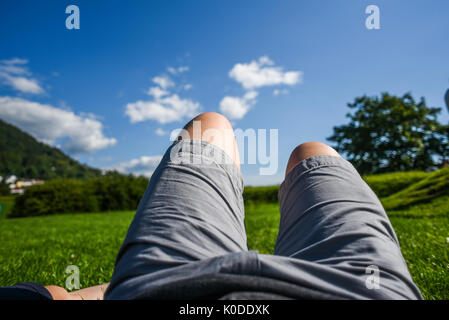 Une photo d'une personne, les jambes allongés sur l'herbe sur un fond de forêt, et vous reposer pendant un jour d'été ensoleillé Banque D'Images