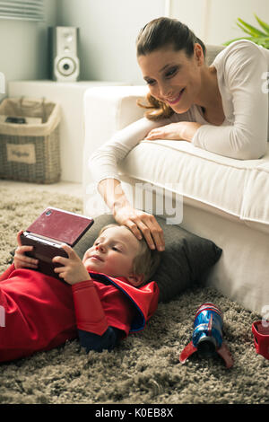 Petit garçon super-héros les jeux vidéo et la mère couchée sur le canapé dans le salon. Banque D'Images