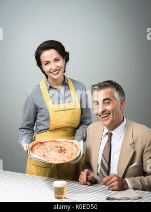 Happy vintage couple having dinner, elle est au service d'une pizza à son mari Banque D'Images