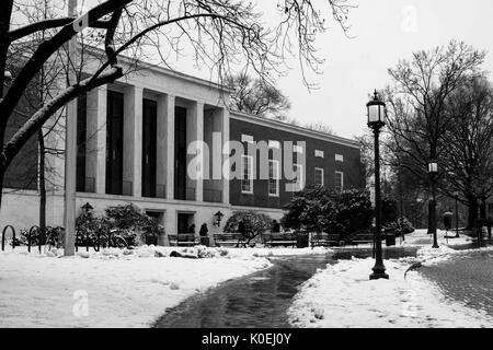 Une vue sur le devant et le plus haut niveau de la bibliothèque Milton S Eisenhower de l'université Johns Hopkins, depuis le chemin en briques pavées et salées au sommet de la « plage » herbeuse, bordée de lampadaires et d'arbres et recouverte de chaque côté de quelques centimètres de neige, Alors que trois personnages sombres approchent de l'entrée, Baltimore, Maryland, 2014. Avec la permission d'Eric Chen. Banque D'Images