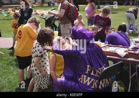 Une femme et un homme portant purple superhero costumes, dont cap et perruque, dessins peinture sur les visages des jeunes enfants au cours de foire de printemps, un carnaval de printemps à la Johns Hopkins University, Baltimore, Maryland, avril, 2014. courtesy eric chen. Banque D'Images