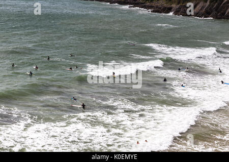 Une scène côtière avec sufers assis sur leurs planches de surf en attente d'attraper une vague à Caswell Bay sur la péninsule de Gower au Pays de Galles, Royaume-Uni Banque D'Images