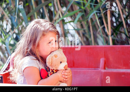 Close up portrait of cute petites filles aux cheveux longs tout en restant assis dans un bateau sur le lac sur une journée d'été belle et ensoleillée et de l'étreindre favorit Banque D'Images