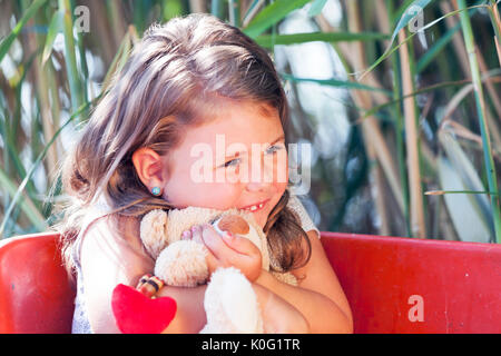 Close up portrait of a cute little Girl with long hair tout en restant assis dans un bateau sur un lac sur une belle journée d'été ensoleillée et serrant son préféré Banque D'Images