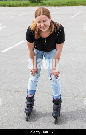 Heureux et smiling young woman riding sur patins à roulettes en parc urbain Banque D'Images