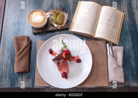 Morceau de gâteau avec des fraises sur une plaque avec une tasse de café sur la table en bois près de vieux livres Banque D'Images