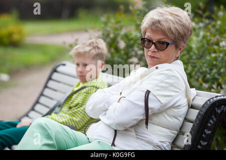 Petit-fils et grand-mère européenne conflit, deux personnes sont assises en pose fermée sur un banc dans le parc Banque D'Images