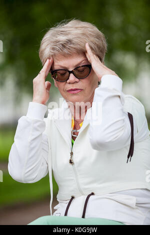 Femme d'Europe senior avec céphalée de tension assis sur le banc après le jogging in park Banque D'Images