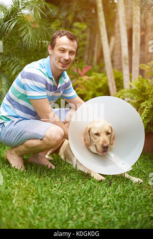 Jeune homme avec le labrador chien dans collier cône Banque D'Images