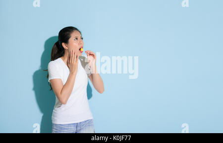 Jolie jolie étudiante debout sur fond mur bleu sucette alimentation et carie dentaire à la position de la zone vide inquiet à propos de de Banque D'Images