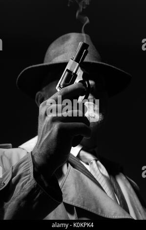 Style années 50 detective posant dans l'obscurité, il est tient une arme et portant un chapeau fedora, personnage de film noir Banque D'Images