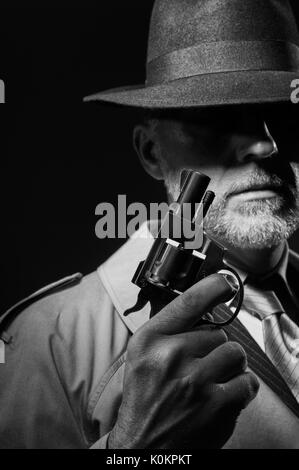Style années 50 detective posant dans l'obscurité, il est tient une arme et portant un chapeau fedora, personnage de film noir Banque D'Images