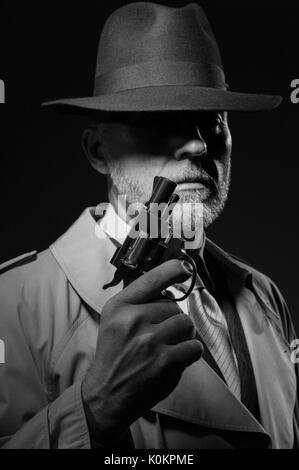 Style années 50 detective posant dans l'obscurité, il est tient une arme et portant un chapeau fedora, personnage de film noir Banque D'Images