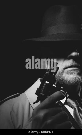 Style années 50 detective posant dans l'obscurité, il est tient une arme et portant un chapeau fedora, personnage de film noir Banque D'Images