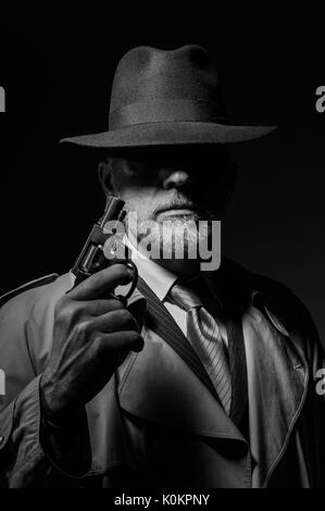 Style années 50 detective posant dans l'obscurité, il est tient une arme et portant un chapeau fedora, personnage de film noir Banque D'Images