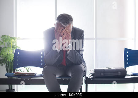 Desperate businessman dans la salle d'attente avec la tête dans les mains, il est en attente d'une entrevue d'emploi, le chômage et l'échec de l'entreprise concept Banque D'Images