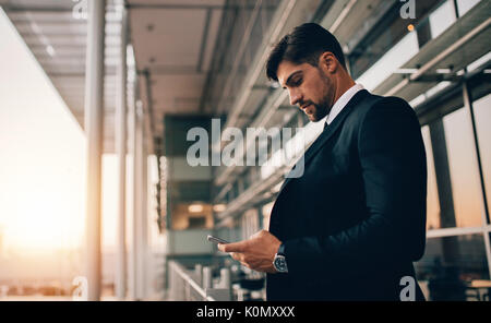 Vue latérale shot of young businessman standing in airport Lounge balcon et à l'aide de téléphone mobile. Direction d'entreprise attend son vol à l'aéroport. Banque D'Images