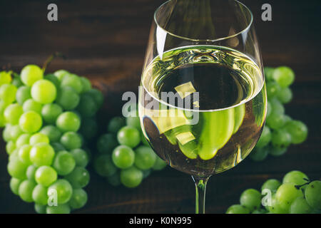 Plein de vin blanc dans des verres à vin avec un tas de raisins verts, sur un fond de bois Banque D'Images